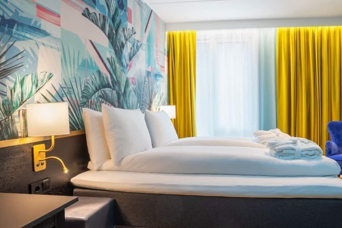 A hotel room with a bed, a desk, a chair, and a lamp.