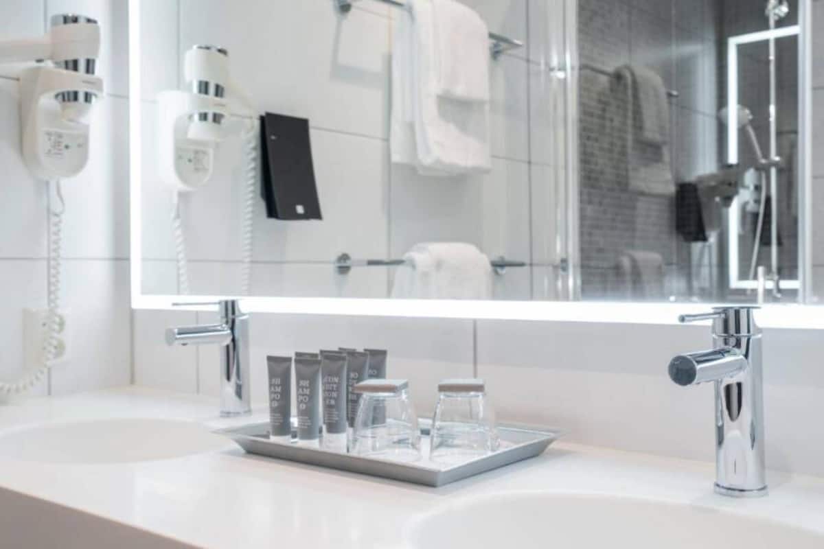 A modern bathroom with a large mirror, a hairdryer, a towel rack, and a sink with toiletries.