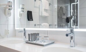 Une salle de bain moderne dotée d’un grand miroir, d’un sèche-cheveux, d’un porte-serviettes et d’un lavabo avec des articles de toilette.