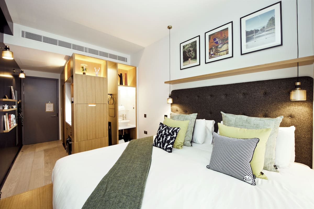A modern hotel room with a large bed, a wardrobe, and a desk area.