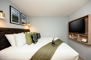 Habitación de hotel moderna con una cama grande, un televisor de pantalla plana y un cabecero de madera.