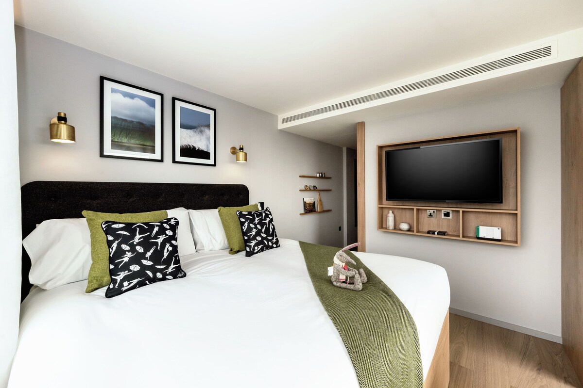 Une chambre d’hôtel moderne dotée d’un grand lit, d’un téléviseur à écran plat fixé au mur et d’une table de chevet avec une lampe.