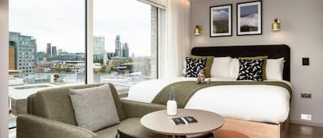 A modern hotel room with a large bed, a sofa, a round table, and a city view.