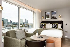 A modern hotel room with a large bed, a sofa, a round table, and a city view.