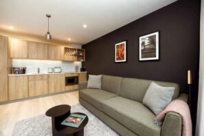 A modern living room with a green sofa, wooden cabinets, and a black floor lamp. - Wilde Aparthotels London Aldgate Tower Bridge (London)