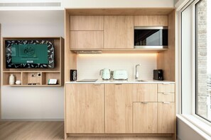 A modern kitchen with wooden cabinets, a built-in microwave, and a window with a view of the city. - Wilde Aparthotels London Aldgate Tower Bridge (London)