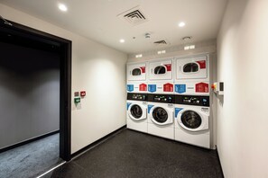 Een wasserette met meerdere wasmachines en drogers, een deur en een lichtschakelaar op de muur.