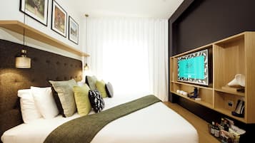 A hotel room with a large bed, a mounted TV, and a shelf with various items.