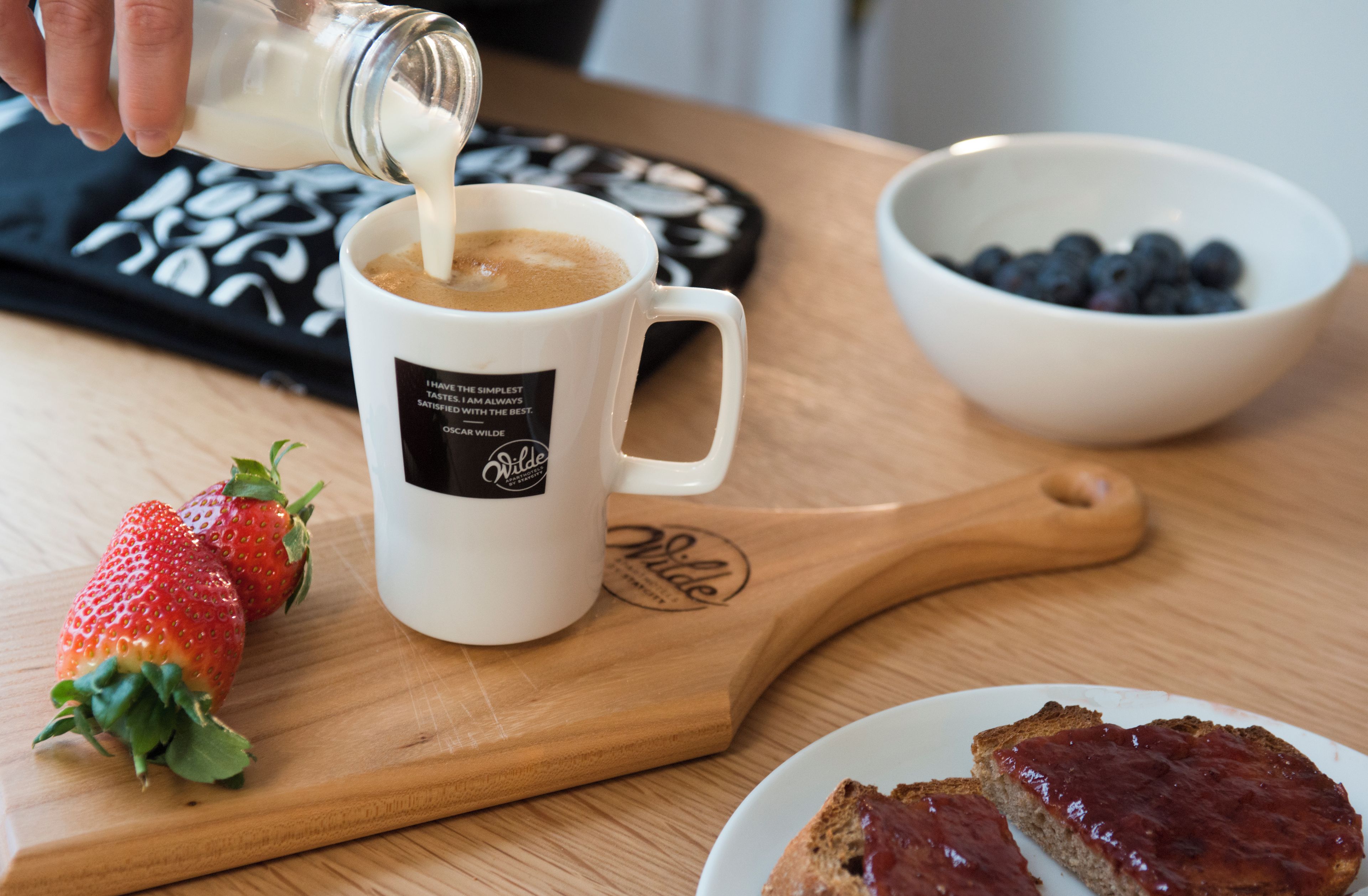 A coffee mug on a wooden board, a bowl of blueberries, and a plate with toast.