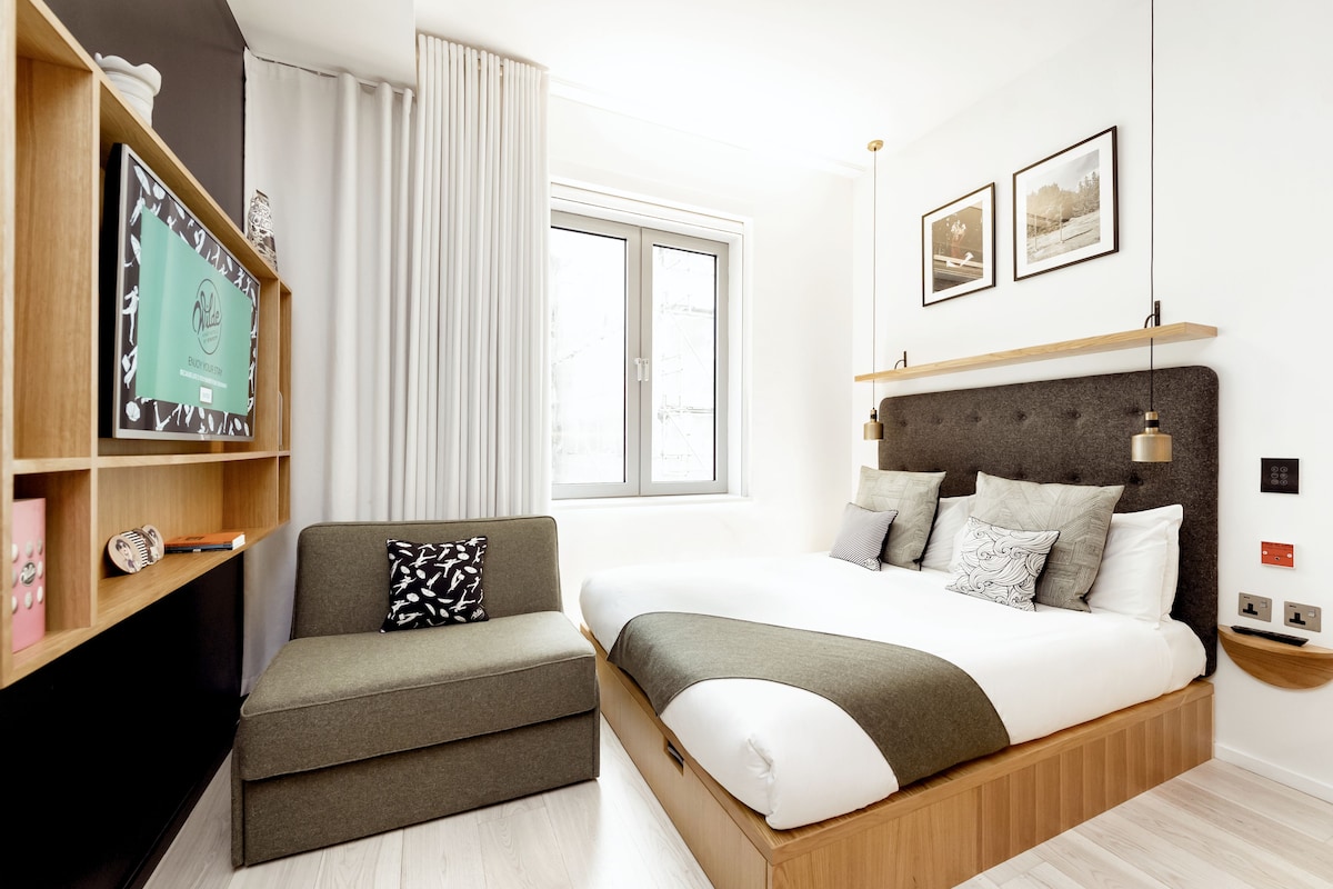 A modern hotel room with a bed, a sofa, a TV, and a window.