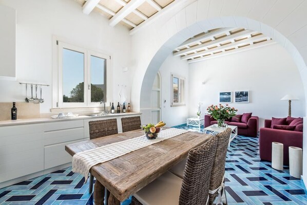 Une cuisine moderne avec un coin repas, comprenant une table en bois, des chaises en osier et un sol carrelé aux motifs bleus et noirs.
