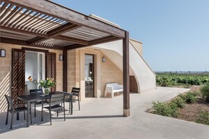 Uma área de estar coberta ao ar livre, com mesa, cadeiras e um banco, e vista para o mar.