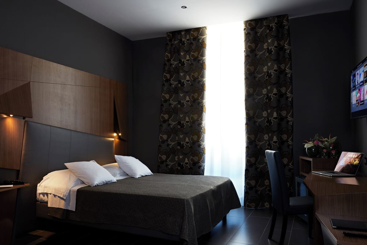 A modern hotel room with a bed, a desk, and a TV.