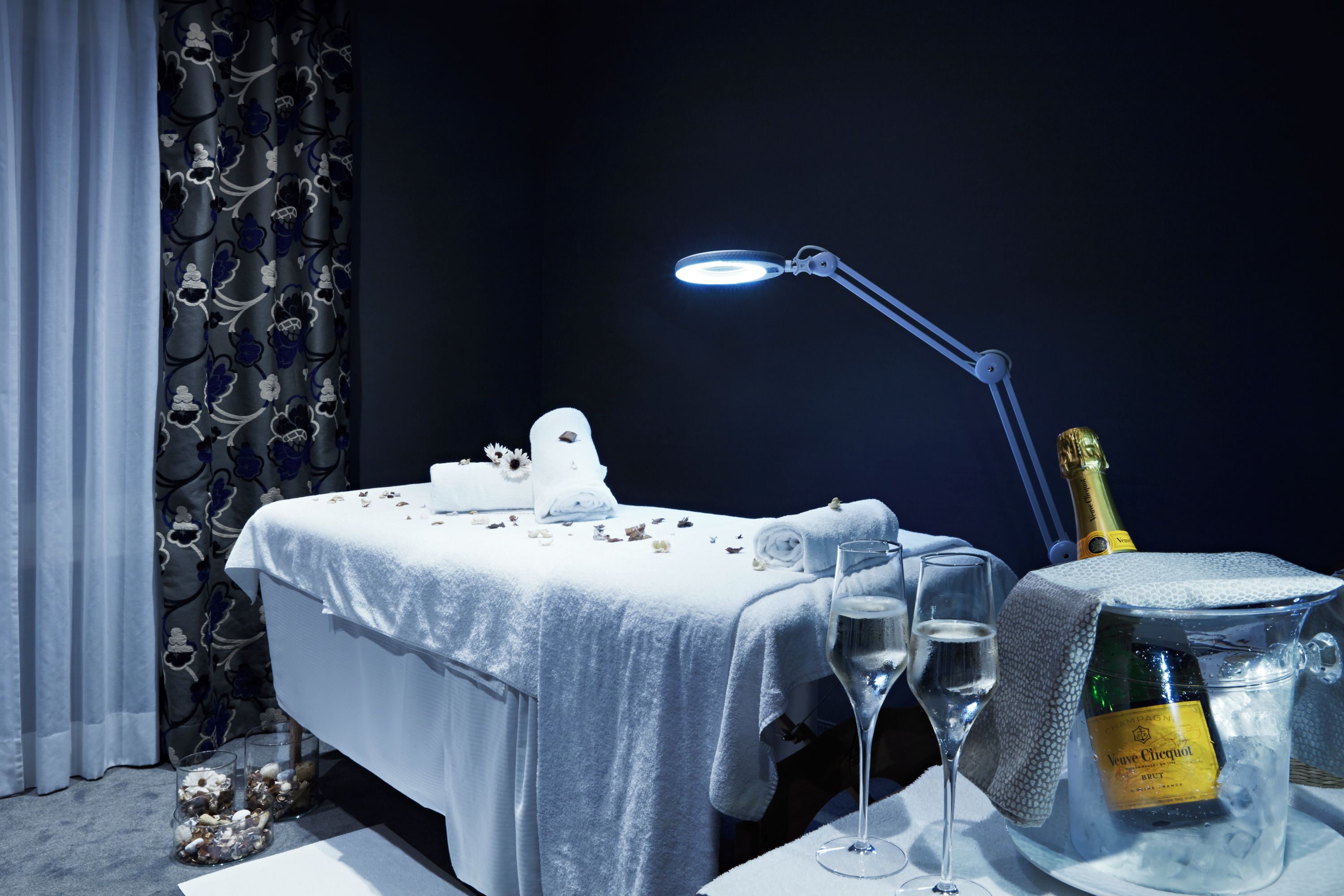 A neatly arranged room with a bed, a bottle of champagne, and two glasses on a table.