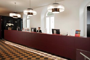 A reception desk with a check-in counter, a receptionist, and a large window. - The Building (Rome)