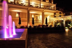 A hotel with a fountain, outdoor seating, and a well-lit balcony. - The Building (Rome)