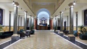 A grand lobby with high ceilings, marble columns, and a patterned floor.