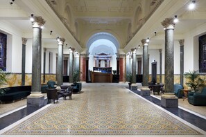 A grand lobby with high ceilings, marble columns, and a patterned floor. - The Building (Rome)