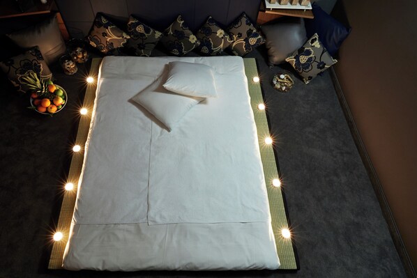 Un letto rifatto con cura, con lenzuola bianche e numerosi cuscini, circondato da una serie di piccole luci luminose lungo il perimetro.