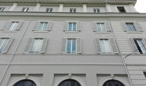 Un edificio de varios pisos con fachada simétrica, amplios ventanales con contraventanas y una entrada central con arco redondeado.