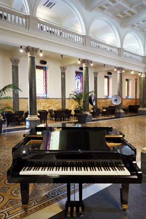 A grand lobby with a grand piano, elegant seating, and a high ceiling with decorative columns. - The Building (Rome)