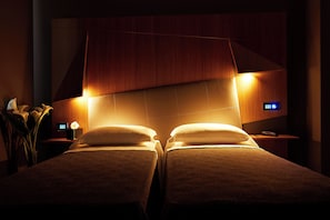 Une chambre d’hôtel avec deux lits, une table de chevet avec une lampe et un panneau de commande fixé au mur.