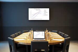 Una sala conferenze con un tavolo rotondo, sedie, un laptop che mostra un grafico di temperatura e uno schermo per proiezioni.