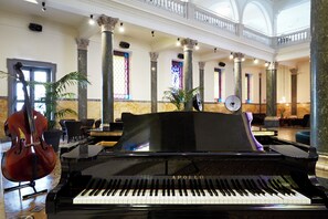 Un maestoso pianoforte a coda in un'ampia hall con soffitti alti e architettura classica, inclusi colonne e vetrate colorate.