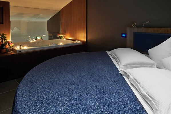 A modern bedroom with a large bed, a bedside table with candles, and a view of the city through a window. - The Building (Rome)