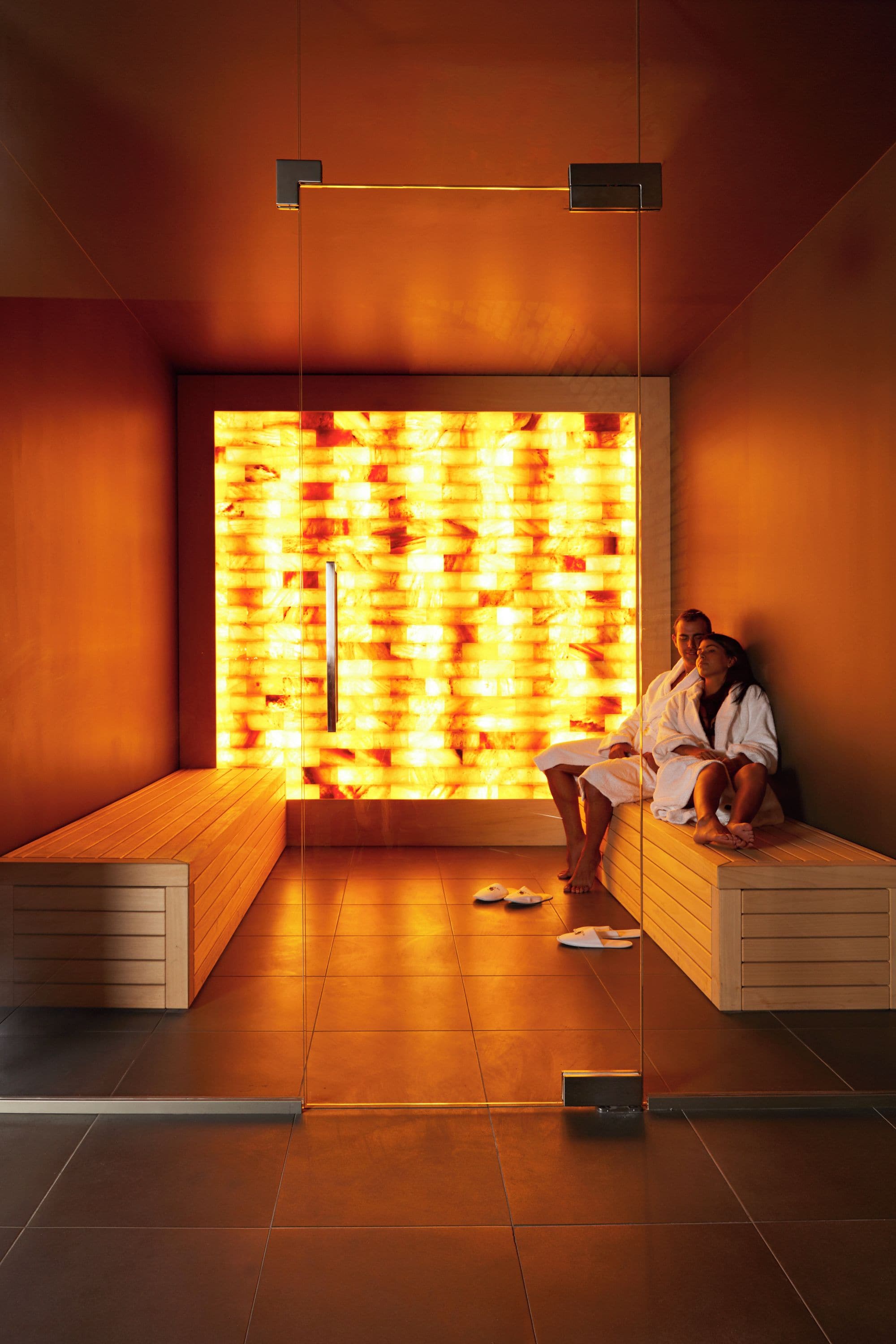 A modern sauna room with wooden benches and a large, illuminated wall.