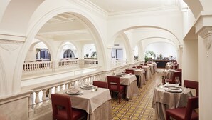 A spacious dining area with high ceilings and arched windows, featuring tables set for dining and a balcony overlooking the interior.