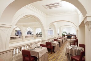 A spacious dining area with high ceilings and arched windows, featuring tables set for dining and a balcony overlooking the interior. - The Building (Rome)
