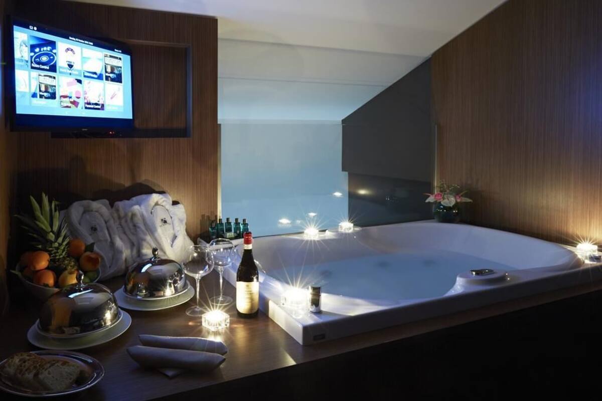 A modern room with a large bathtub, a television mounted on the wall, and a table with towels, fruits, and bottles.