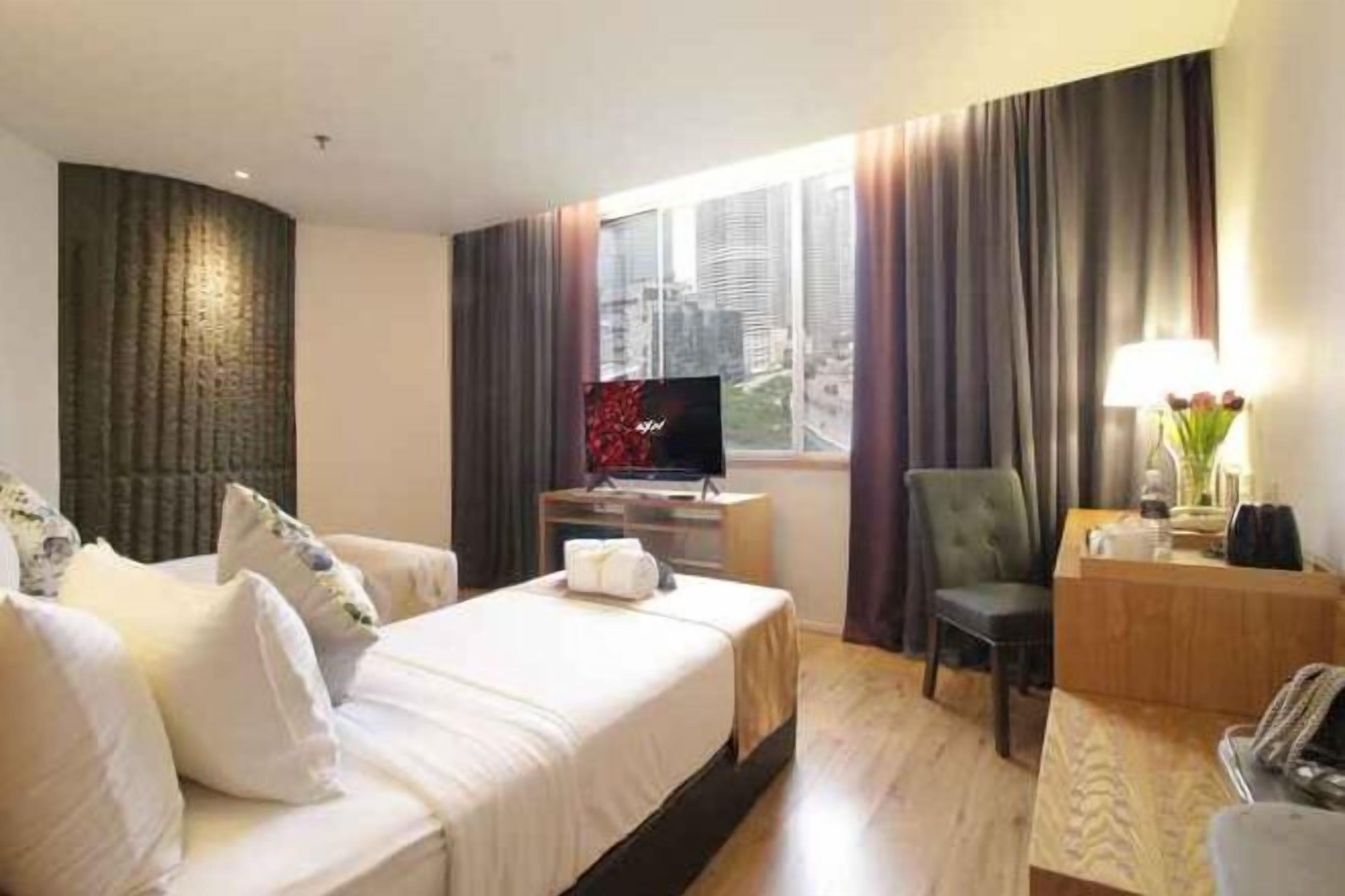 Habitación de hotel con cama, escritorio con computadora, silla, televisor y ventana con cortinas.