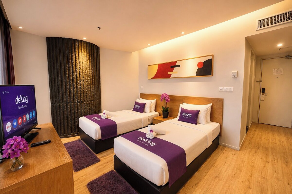 A hotel room with two beds, a TV, and a desk with a flower vase.