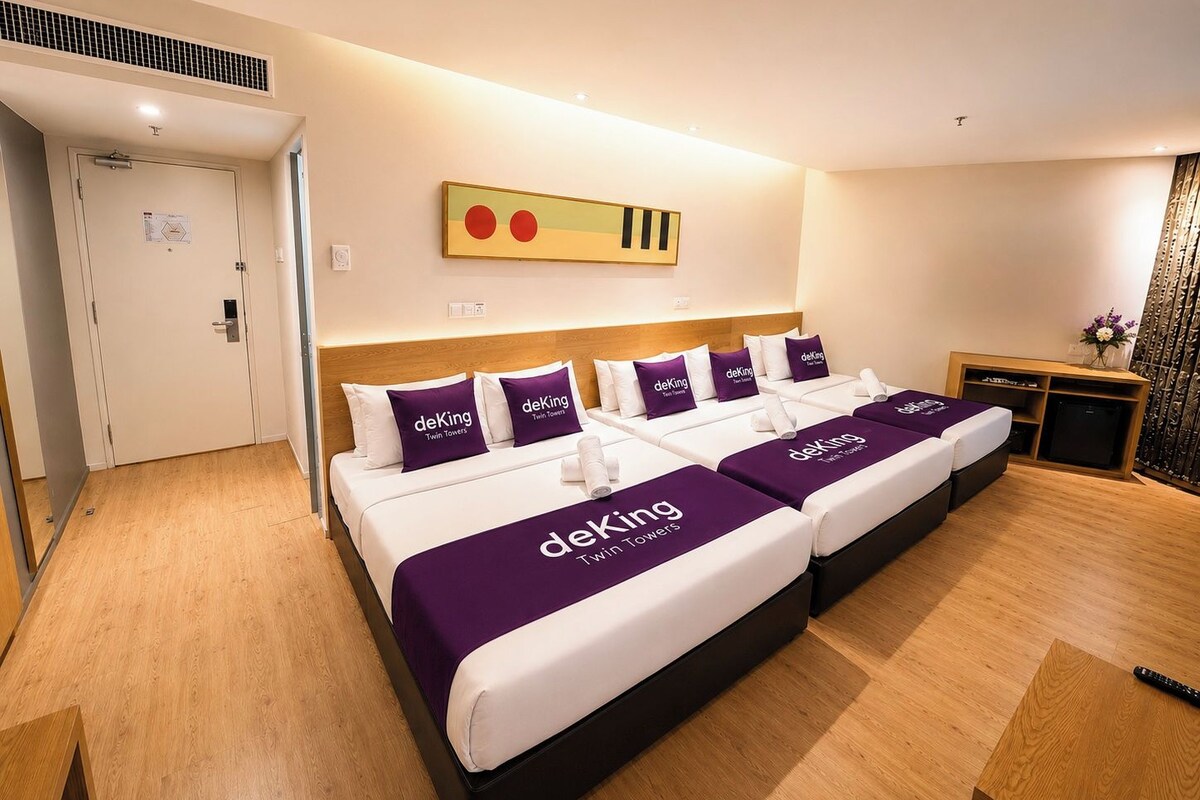 A hotel room with two beds, each with a purple bedspread and pillows labeled 'deKing Twin Towers.'