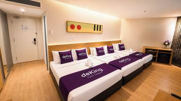A hotel room with two beds, each with a purple bedspread and pillows labeled 'deKing Twin Towers.'