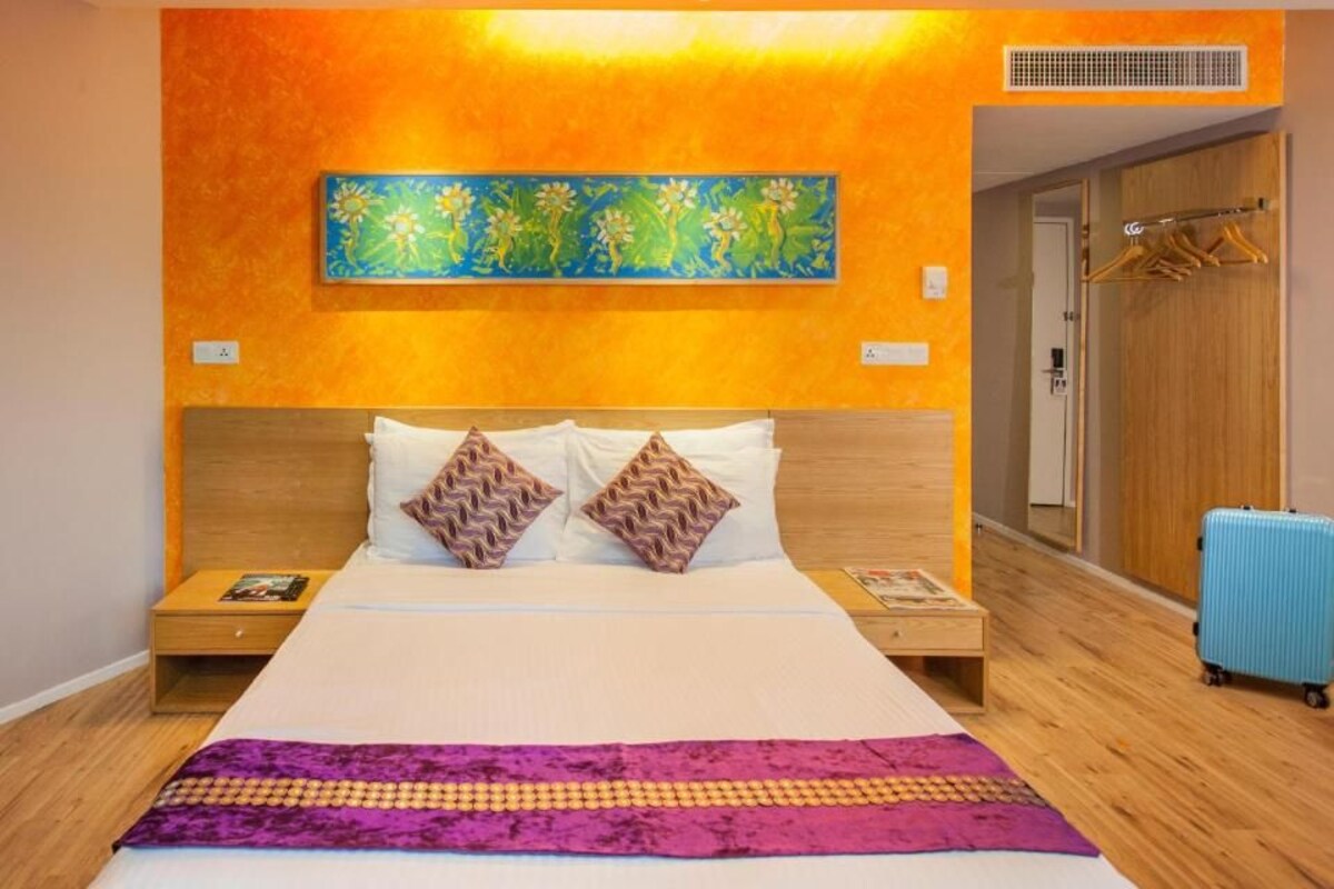 A hotel room with a large bed, two nightstands, a blue suitcase, and a colorful painting on the wall.