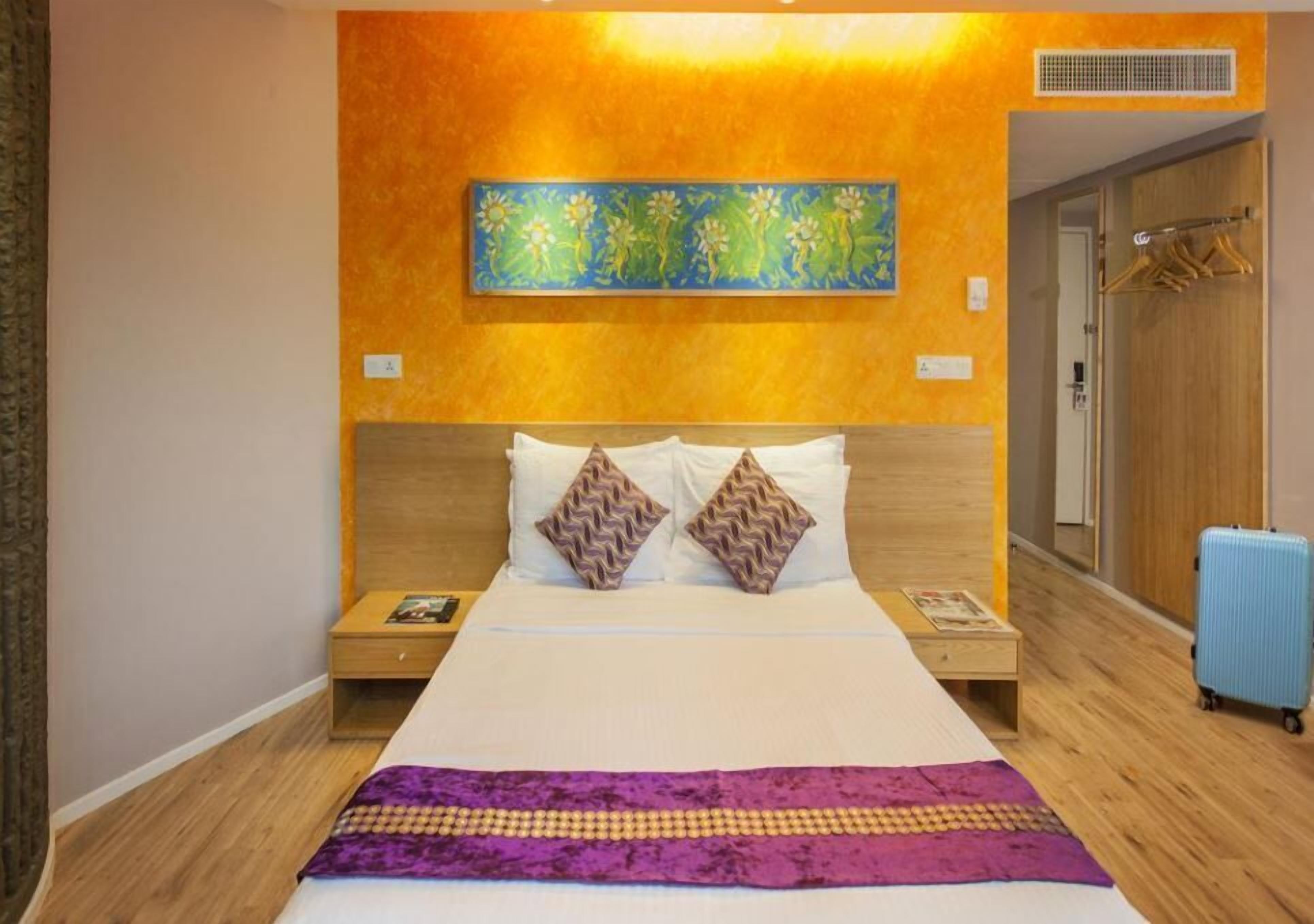 Een hotelkamer met een groot bed, een houten hoofdbord, twee nachtkastjes, een kunstwerk aan de muur en een koffer.