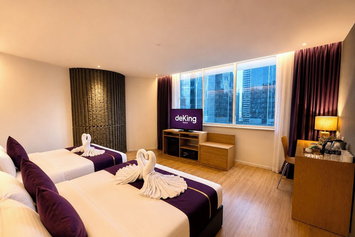 A hotel room with two beds, a TV, a desk, and a view of the city.