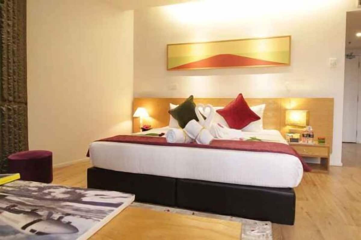 A hotel room with a bed, bedside tables, a painting on the wall, and a wooden floor.
