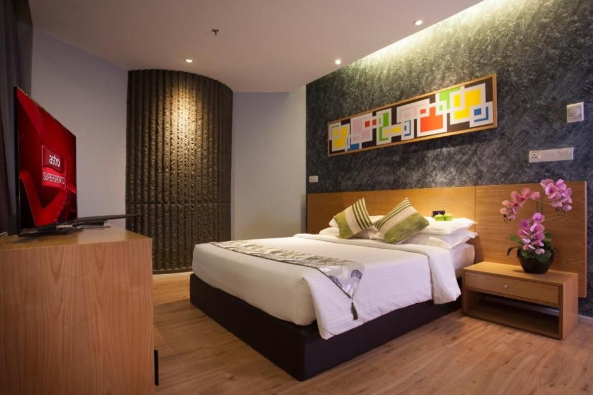 A modern hotel room with a large bed, bedside tables, a TV, and a decorative wall piece.
