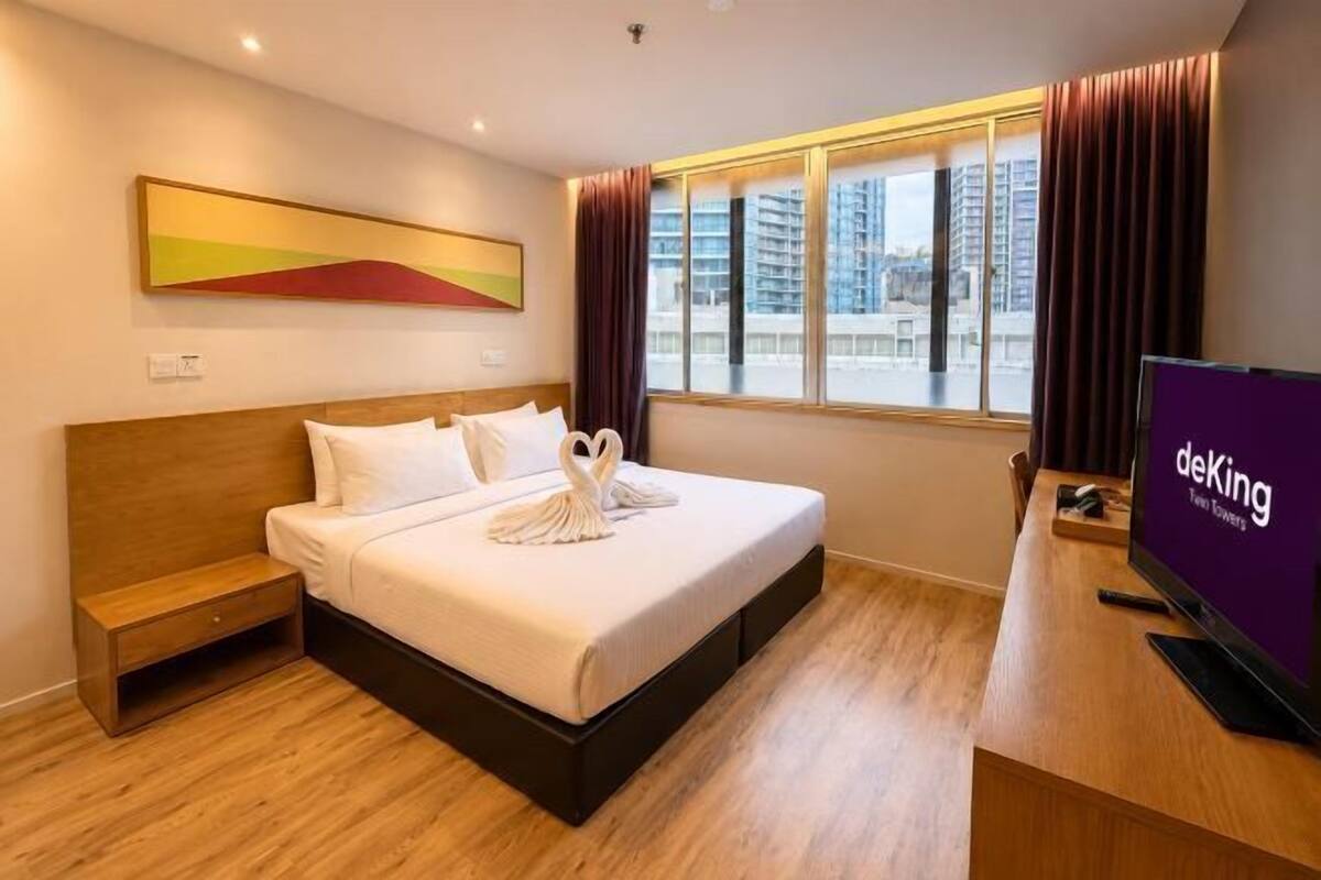 Ein Hotelzimmer mit Bett, Schreibtisch, Fernseher, Fenster mit Vorhängen und einem Bild an der Wand.