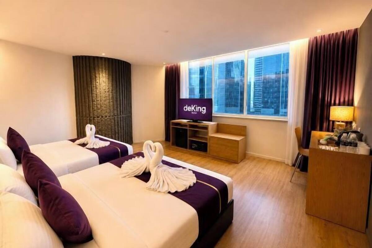 Ein Hotelzimmer mit zwei Betten, einem Fernseher, einem Schreibtisch und einem Fenster mit Blick auf die Stadt.
