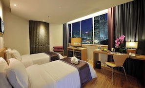 A hotel room with two beds, a desk, a chair, a TV, and a view of a cityscape at night. - de King Hotel Klcc (Kuala Lumpur)