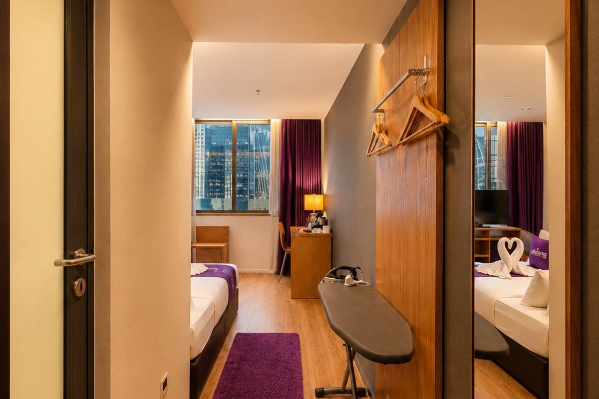 Une chambre d’hôtel avec un lit, un bureau, un miroir, une fenêtre avec des rideaux et une vue sur la ville.