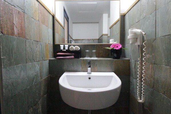 Ein Badezimmer mit einem weißen Waschbecken, einem Spiegel und einem an der Wand befestigten Fön.