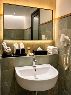 Une salle de bain avec un lavabo blanc, un miroir, un porte-serviettes, un sèche-cheveux et des articles de toilette.