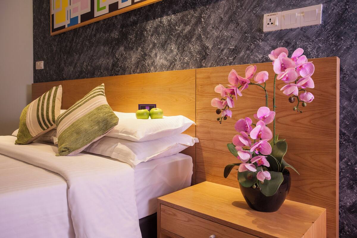 Ein ordentlich bezogenes Bett mit gestreifter Bettwäsche, ein Nachttisch mit einer Orchidee im Topf und ein Holz-Kopfteil.