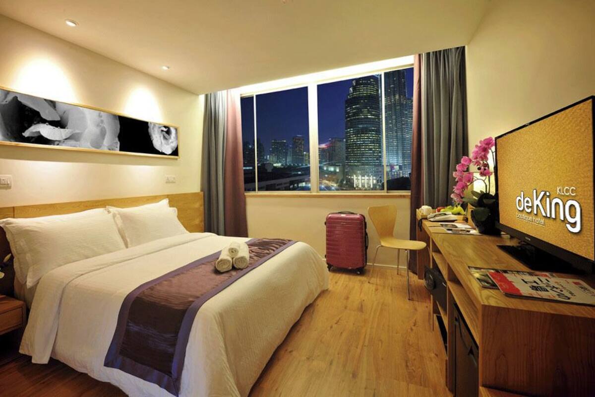 Ein Hotelzimmer mit Bett, Schreibtisch, Fernseher, Fenster mit Stadtblick und einem Bild an der Wand.